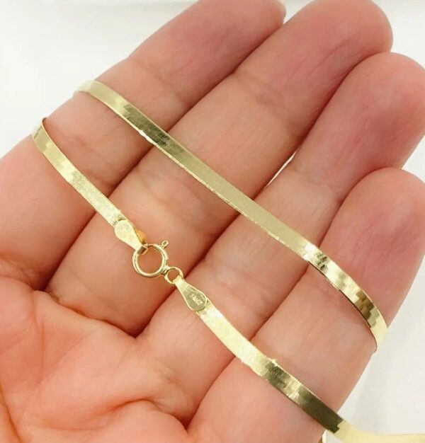 A hand holding a gold chain in front of the camera.