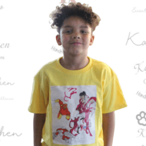 A young boy wearing a yellow shirt with a painting on it.
