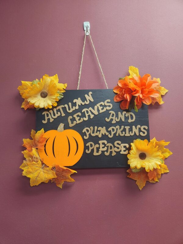 A sign hanging on the wall with autumn leaves and pumpkins.