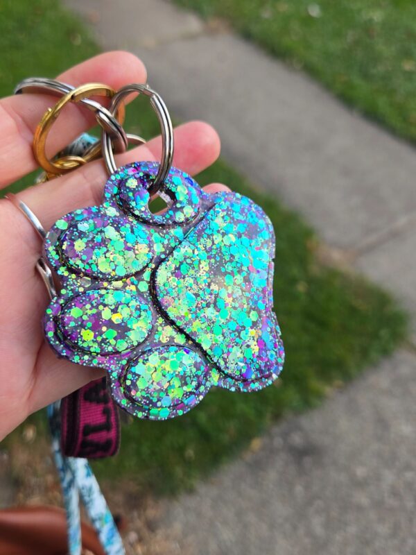 A hand holding up a key chain with a dog paw print.