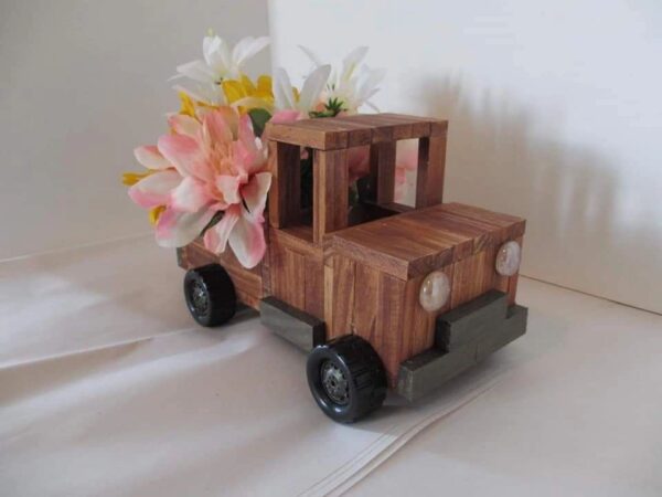 A wooden toy truck with flowers in the back.