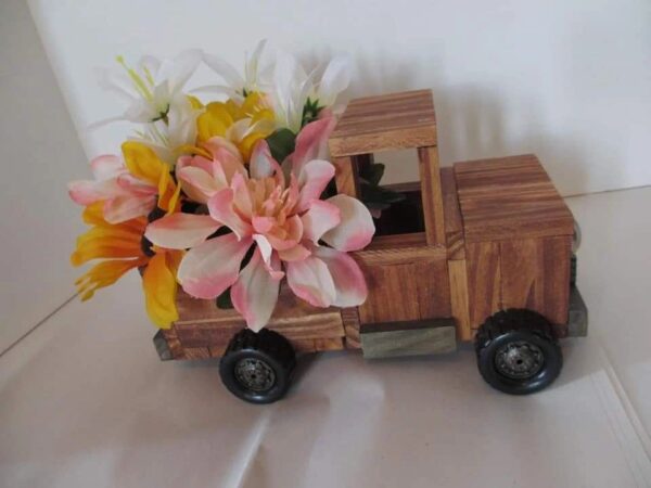 A wooden toy truck with flowers in the back.