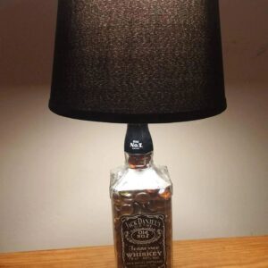 A bottle lamp with a black shade on top of a table.