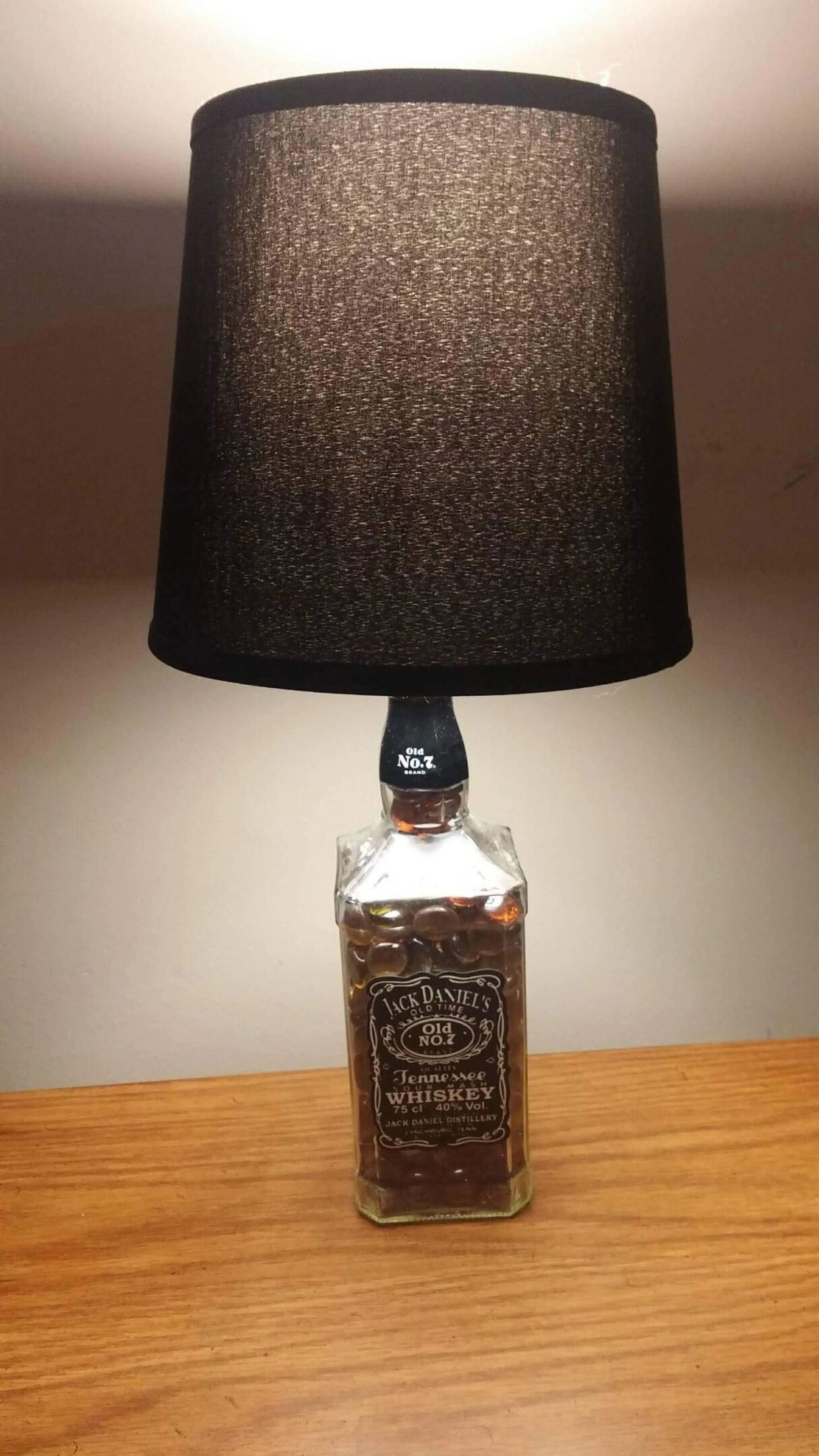 A bottle lamp with a black shade on top of a table.