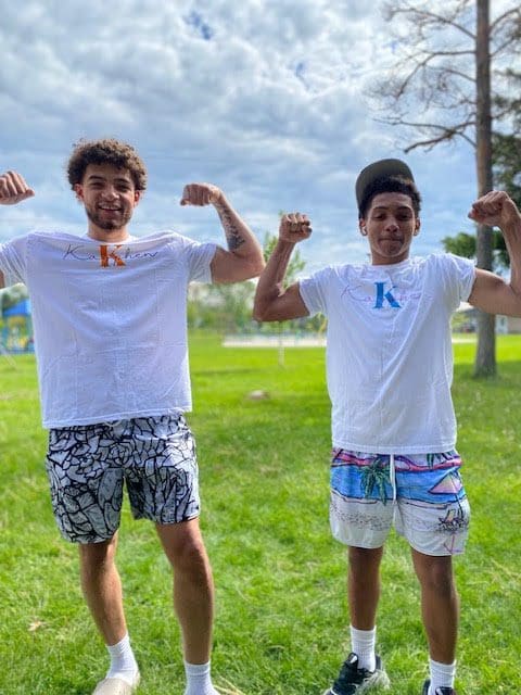 Two men flexing outdoors on grass.