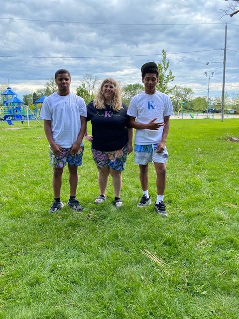 Three people standing on grass, smiling outdoors.