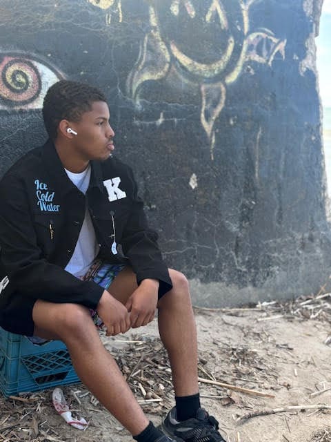 Young man sitting by graffiti wall.