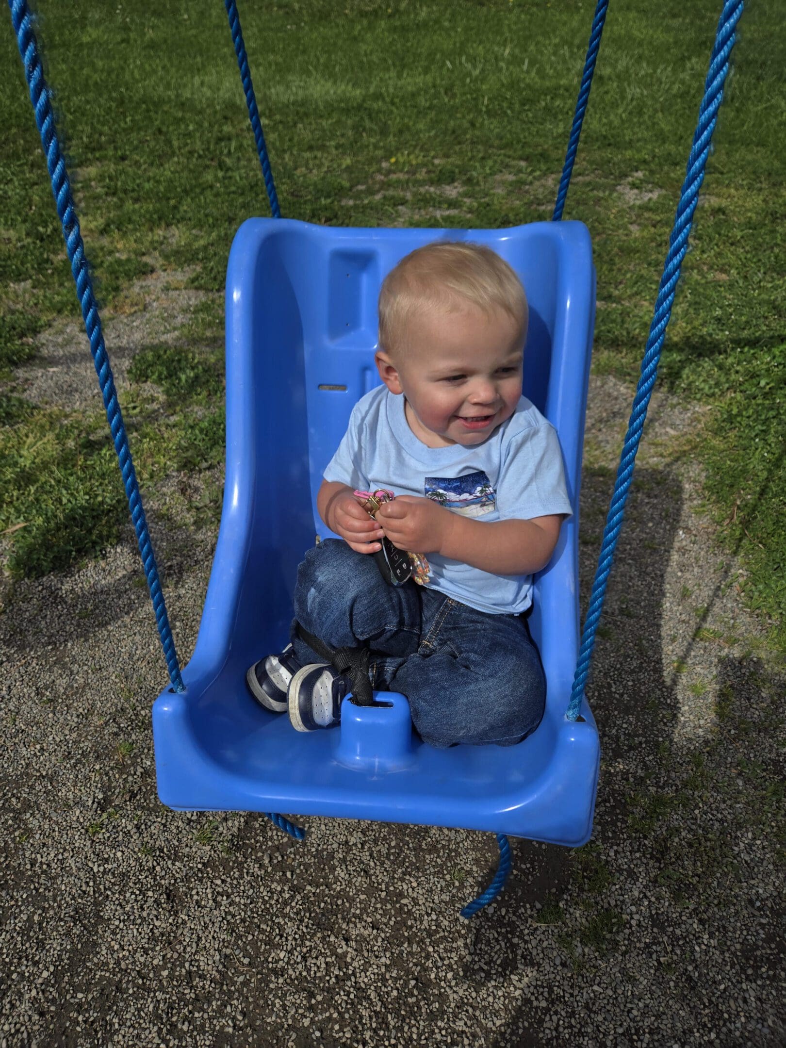 Toddler sitting on a blue swing outdoors.